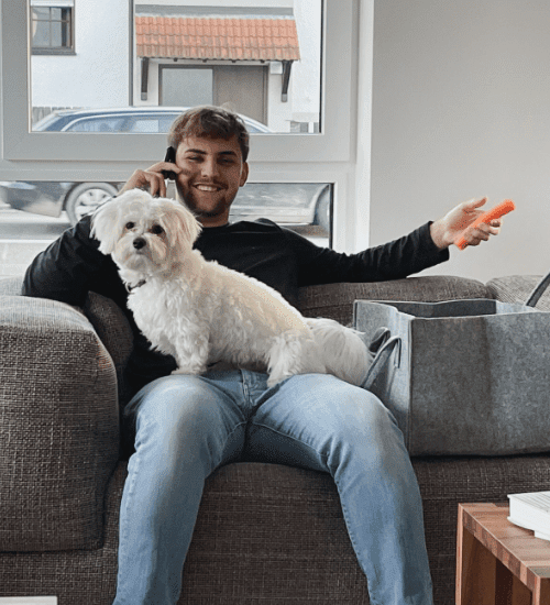 Das ist Elias auf einer Couch mit Hund Gino. Beide sind feste Teile des Teams bei Home & Living Immobilien, Ihr Immobilienmakler im Raum Schorndorf